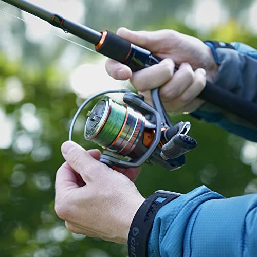 Nahaufnahme eines Anglers mit der Mitchell Traxx MX2 Lure Spinnruten und Rollen Combo, die perfekt zum Angeln von Hecht, Barsch, Zander und Forelle geeignet ist. Die Angelrute hat ein schwarzes Design mit orangefarbenen Akzenten, gehalten von einer Person in einem blauen Outdoor-Outfit. Im Hintergrund ist eine natürliche Gewässerlandschaft zu sehen.